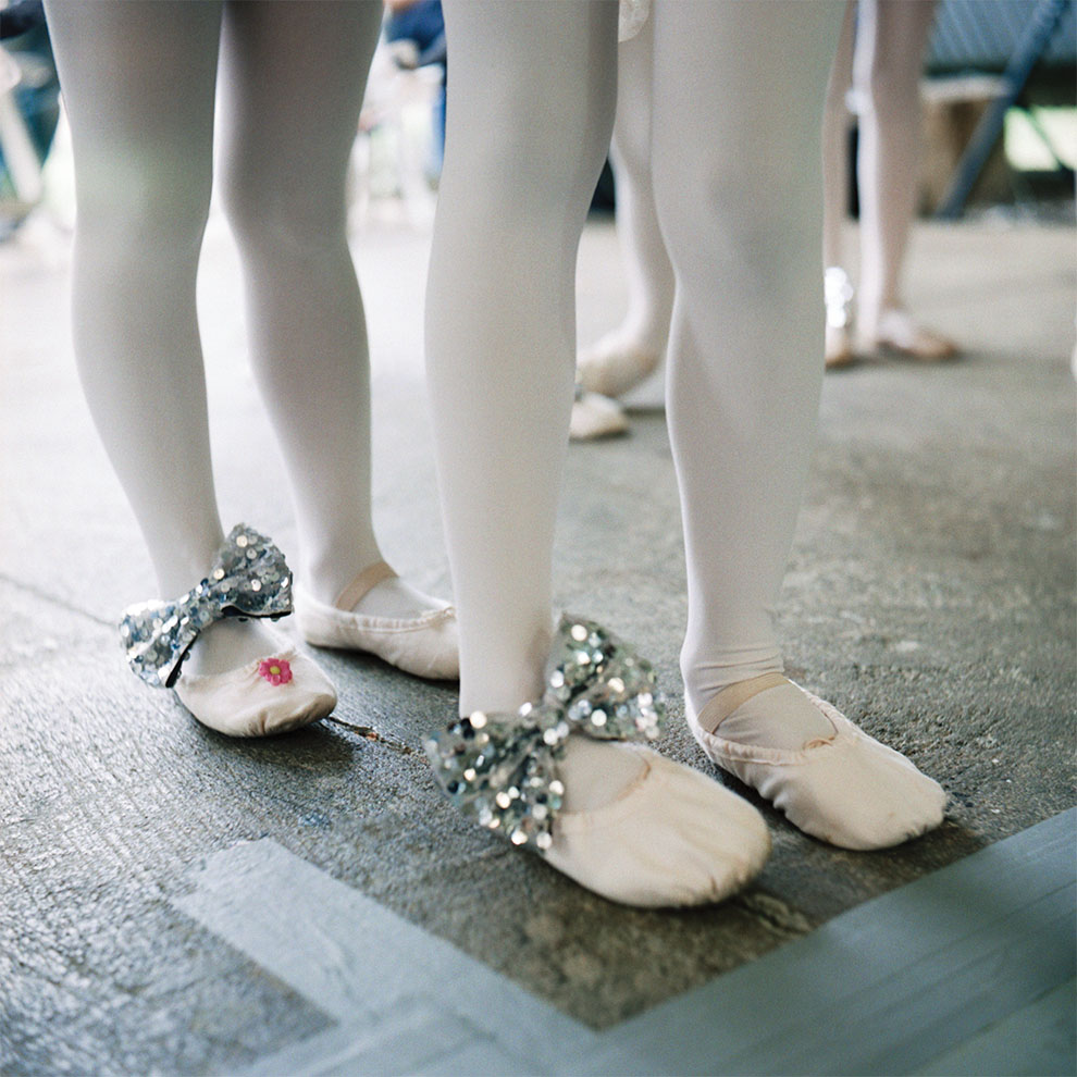 close-up of young ballet dancers' legs in pink tights and pink soft shoes with silver bows.