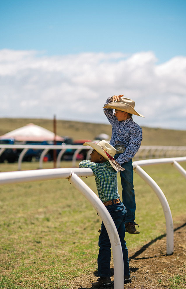 a man and son in cowboy hats stand waiting for the race at the ranch.