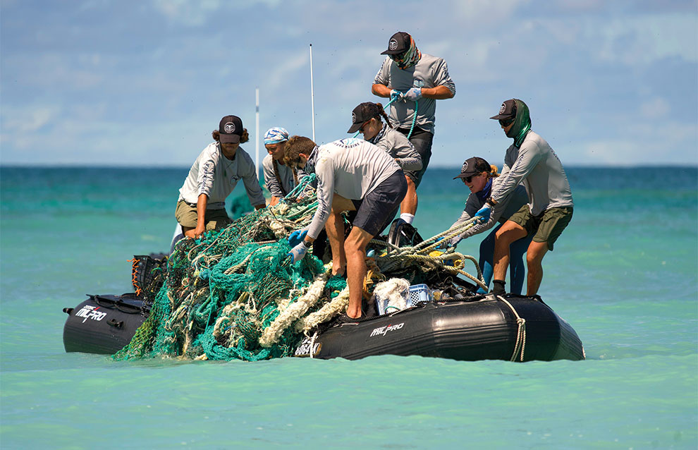 group of people on top of small raft dragging a blue net from the water onto the boat.