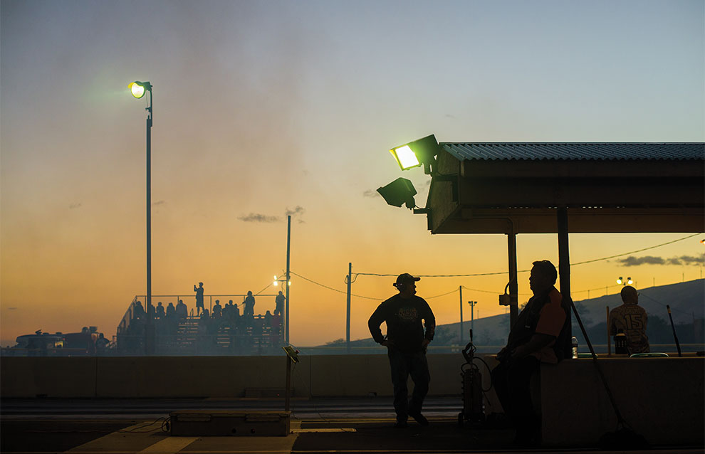 silhouette of three men standing by race track and outdoor cover with sunset in background.
