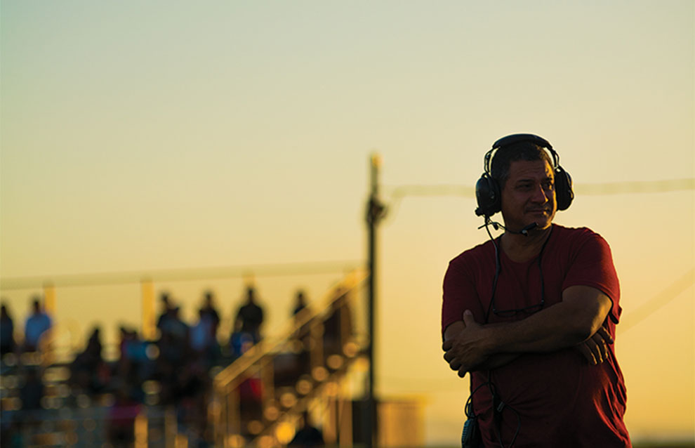 silhouette of man with headphones and a microphone attachment in red shirt against a sunset background